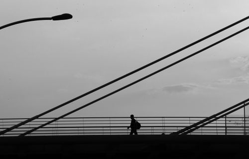 Free Black and white silhouette of an individual walking on a suspension bridge under a streetlamp. Stock Photo