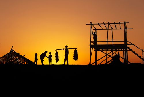 Free Silhouetted workers constructing and carrying goods under a vibrant sunset. Stock Photo