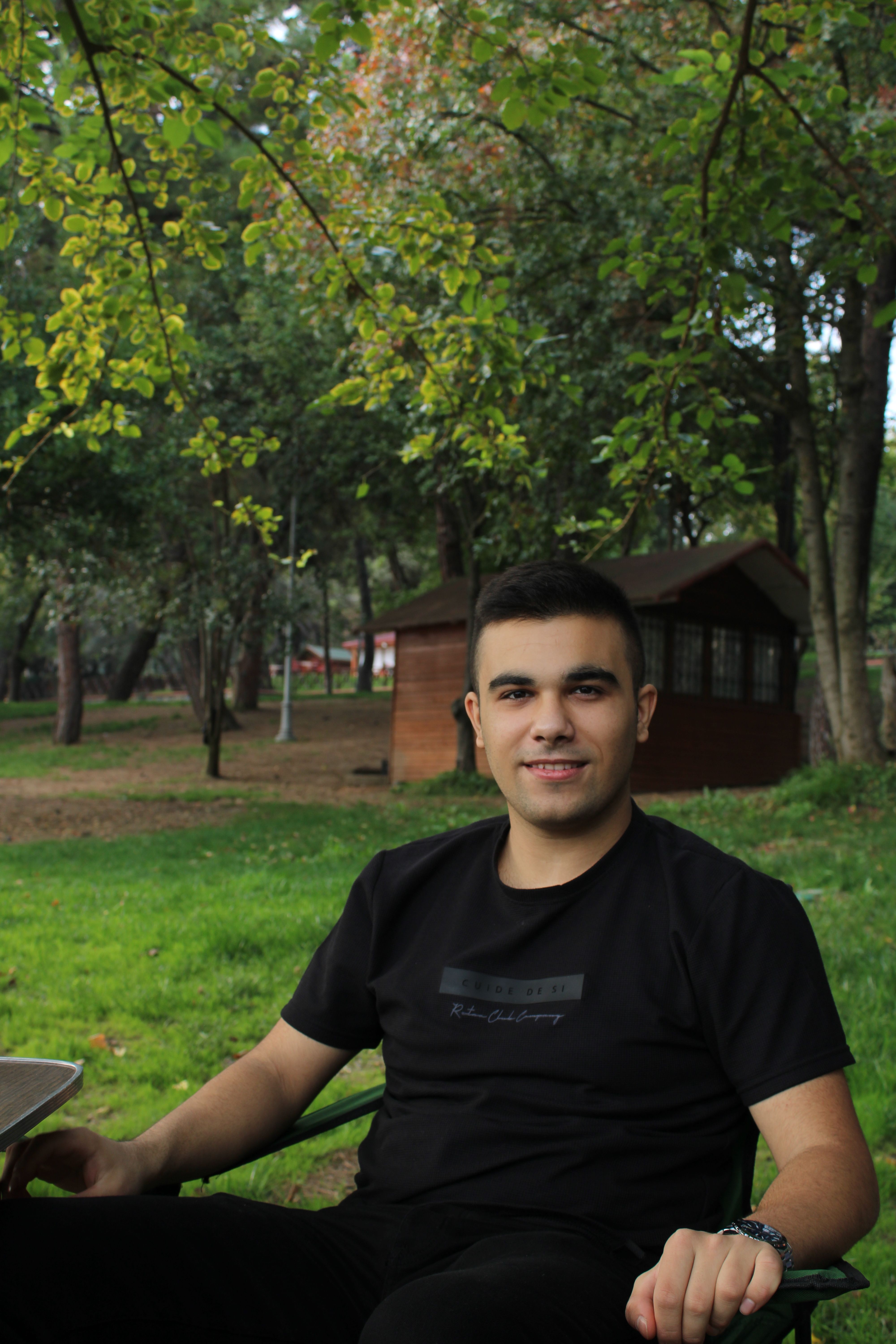 Casual portrait of a young man sitting outdoors in a serene garden setting, showcasing relaxation.