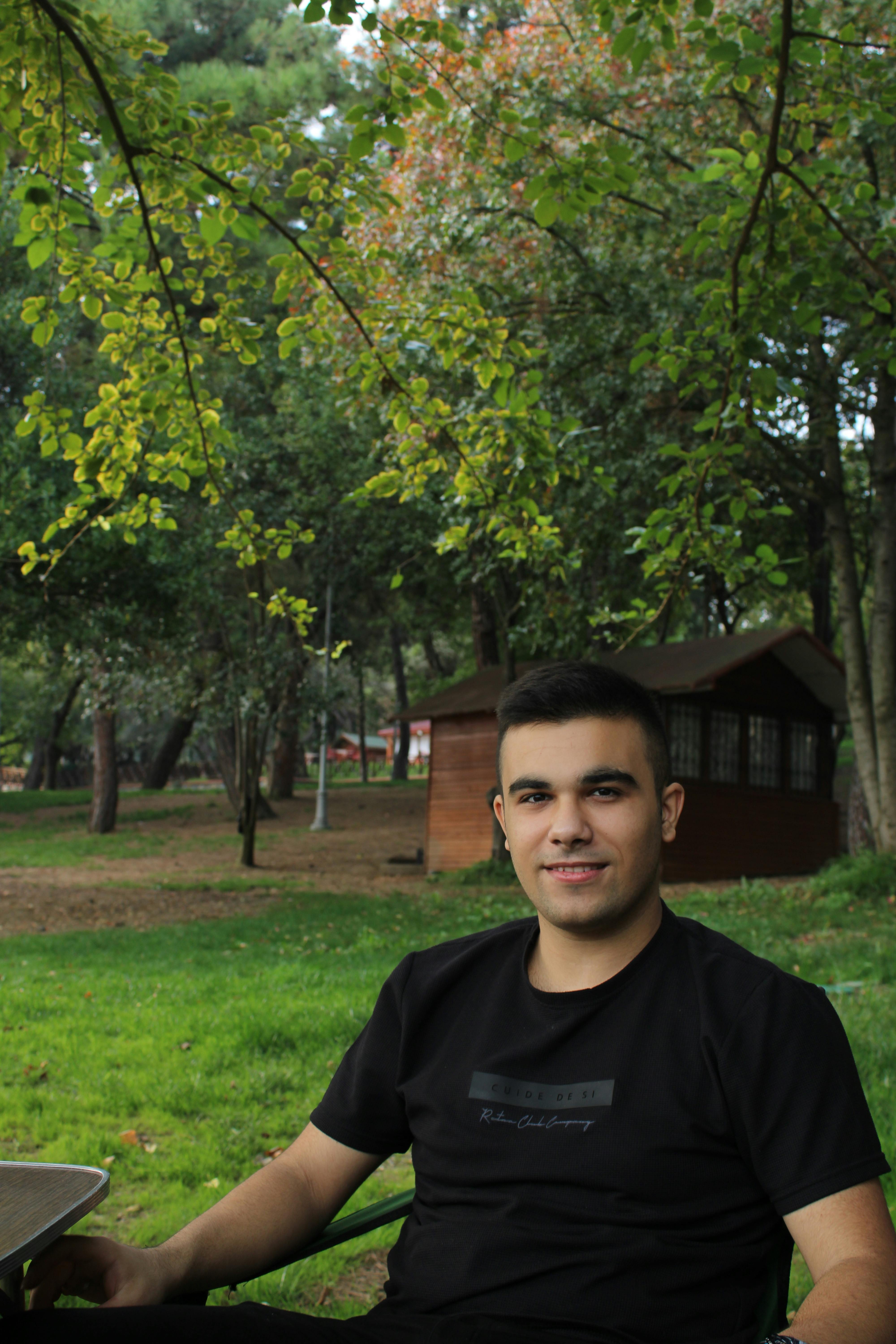 Young man enjoys a serene moment in a lush green park with a wooden cabin backdrop.