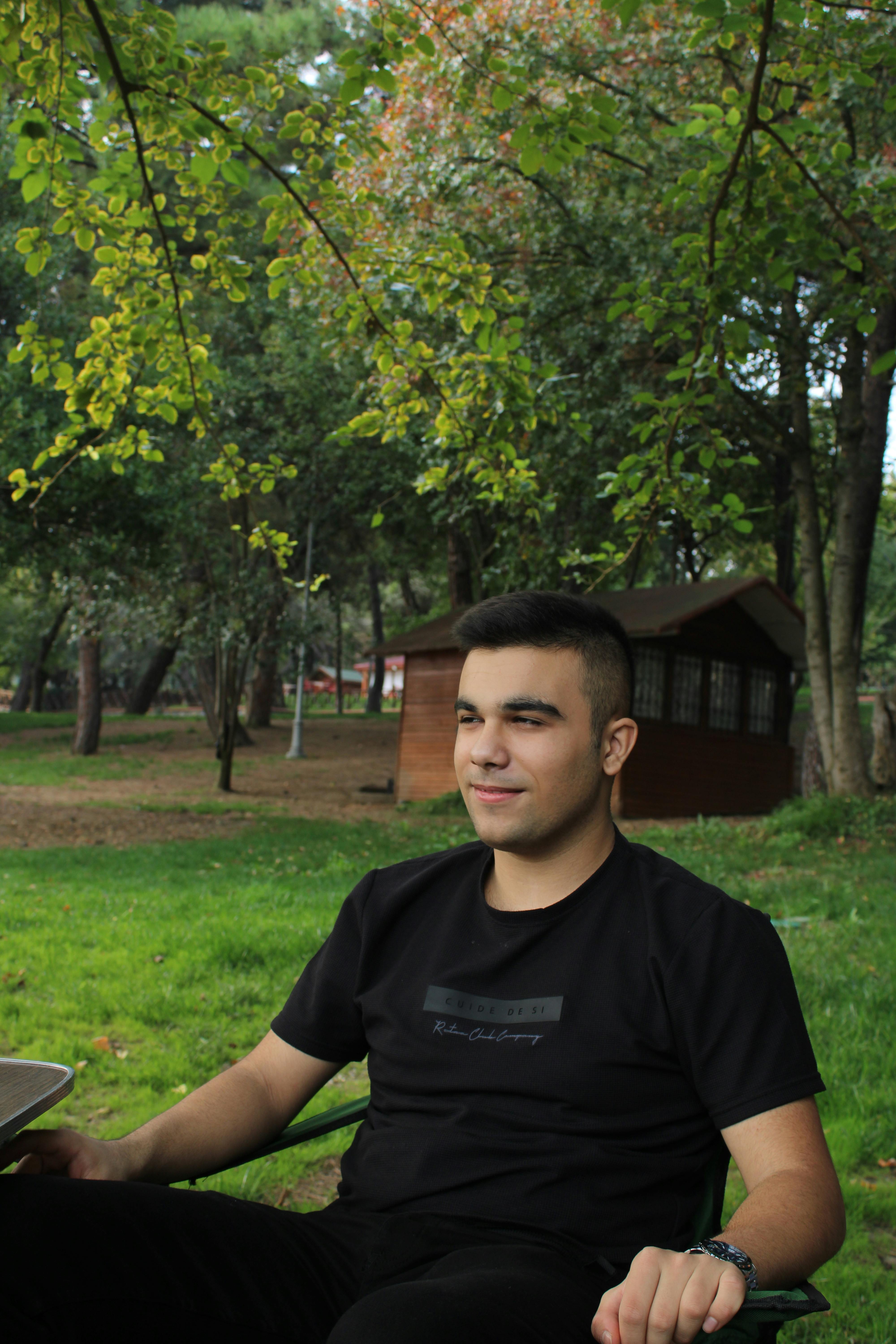 A young man enjoying a peaceful moment seated in a lush green park with trees.