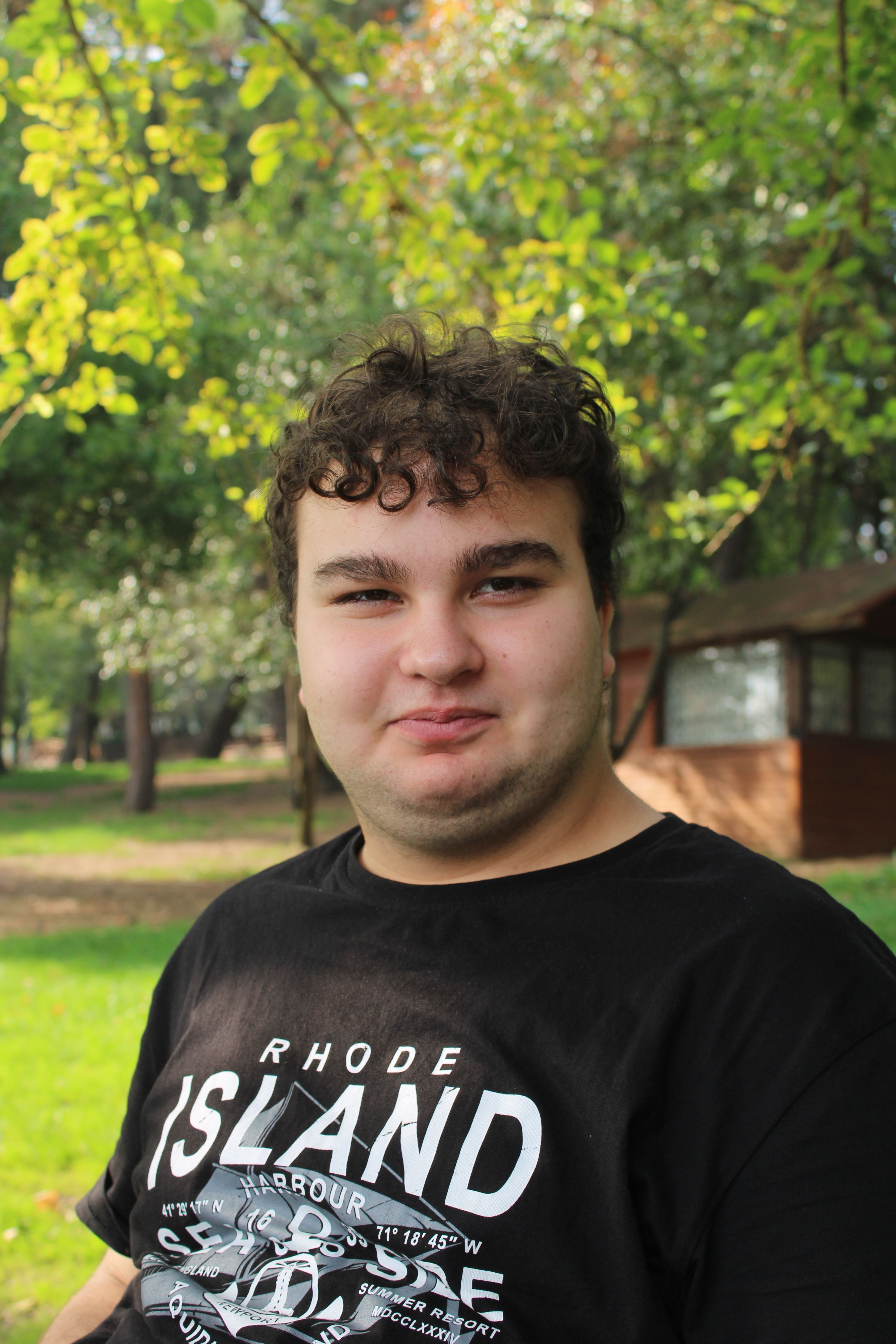 Portrait of a young man in a park with green trees and sunlight.