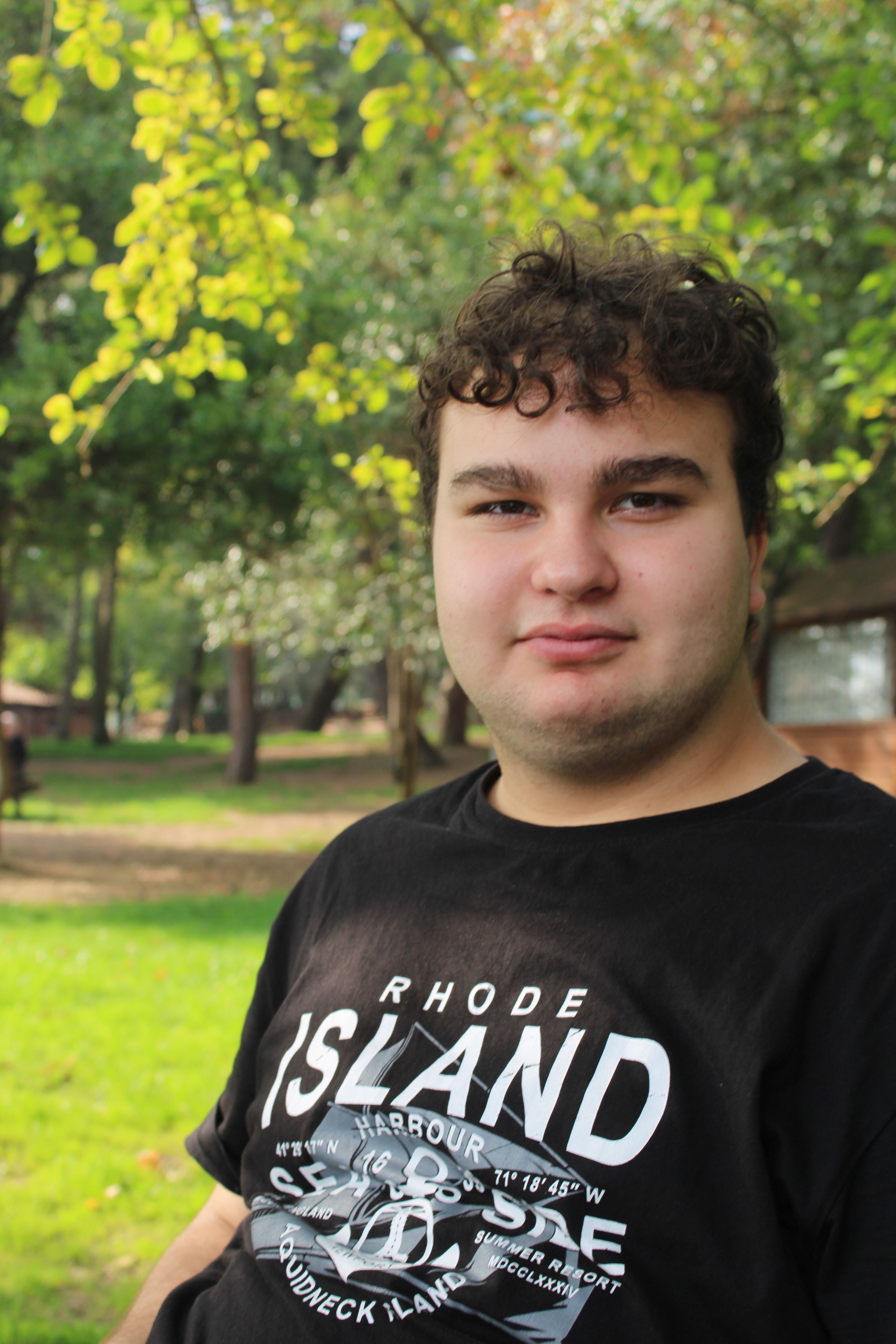 Portrait of a young man sitting outdoors in a lush green park on a sunny day.