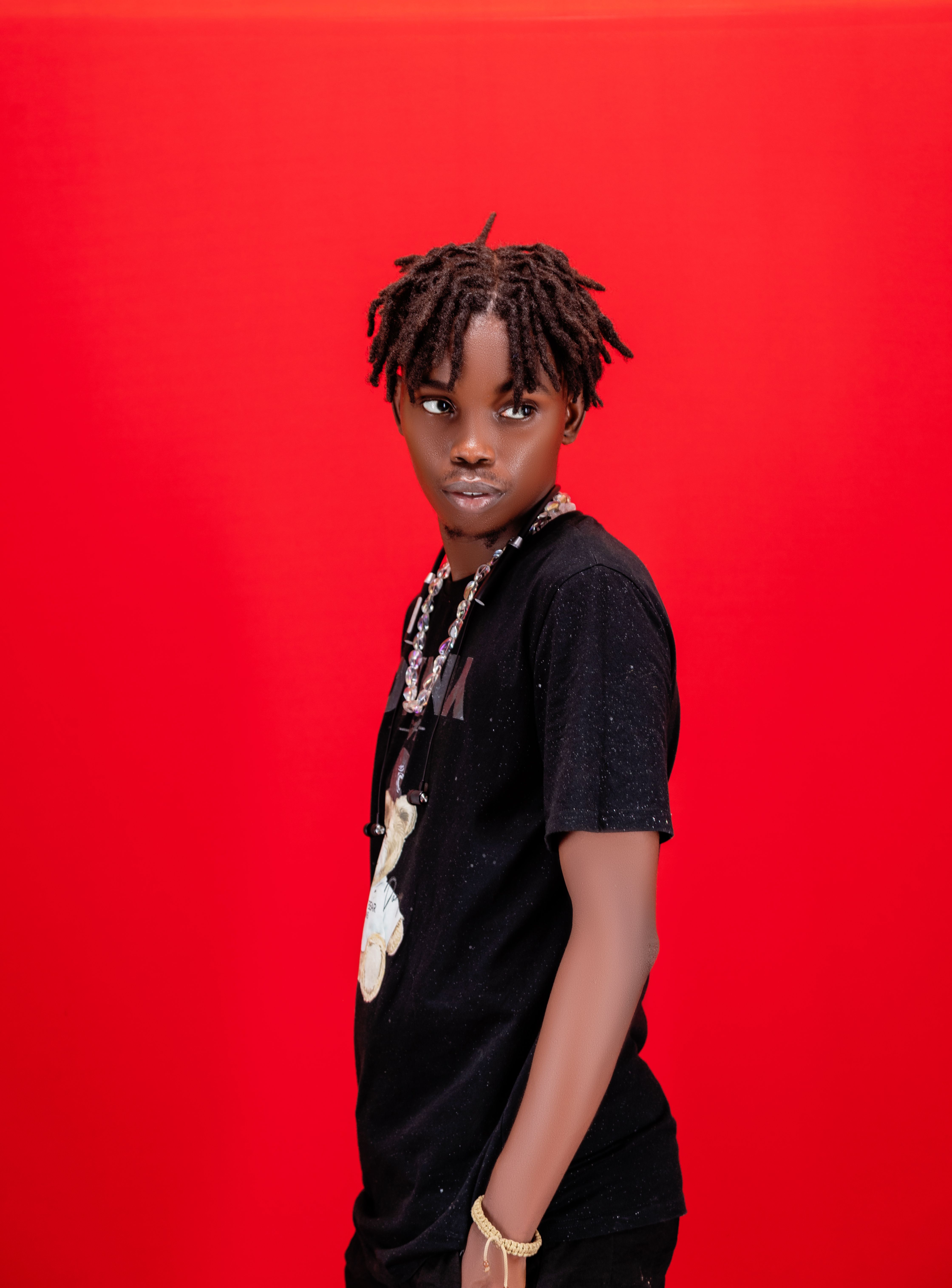 Young adult with dreadlocks striking a pose against a vibrant red backdrop, exuding confidence and style.