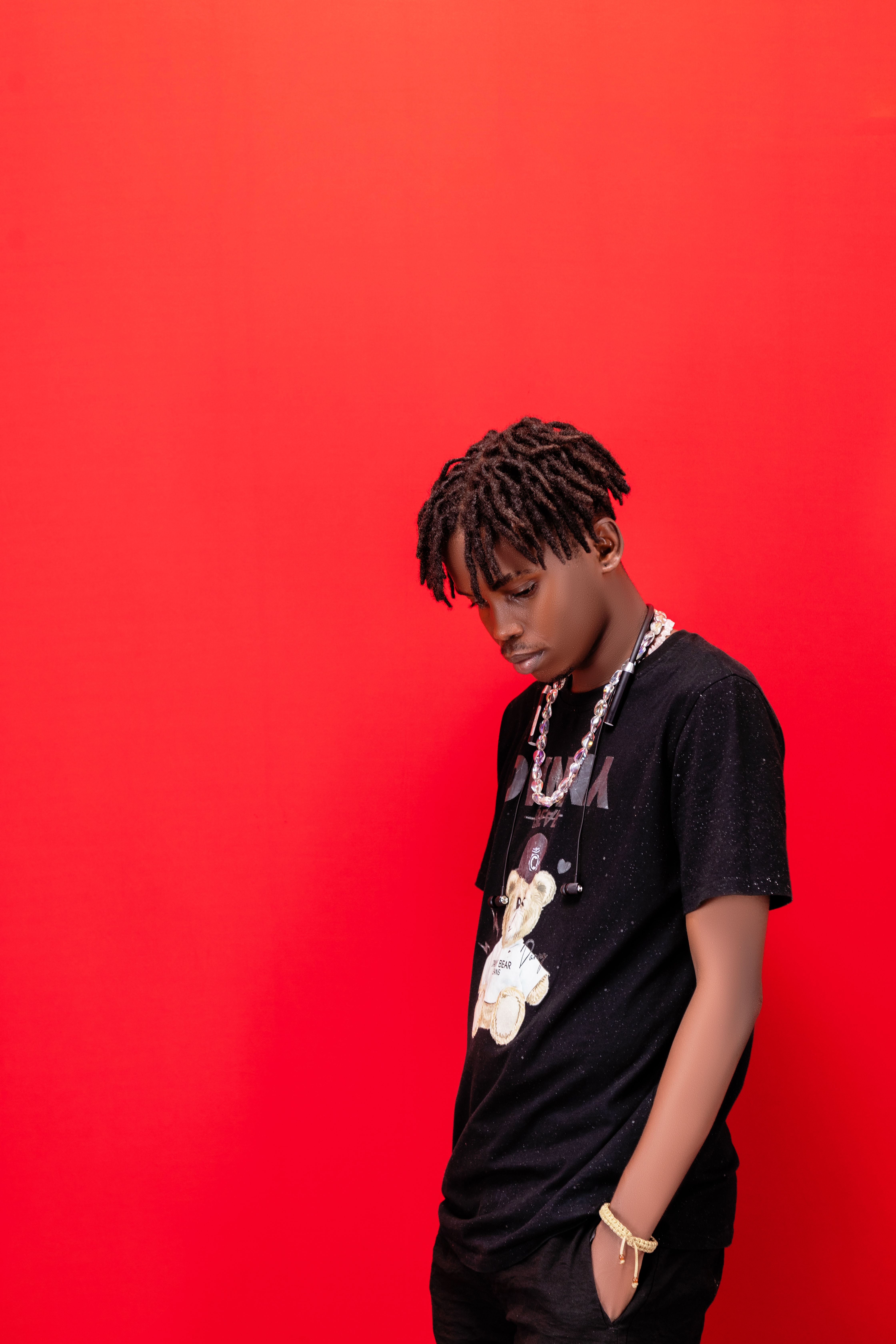 Stylish young adult standing against a bold red background, wearing trendy attire.