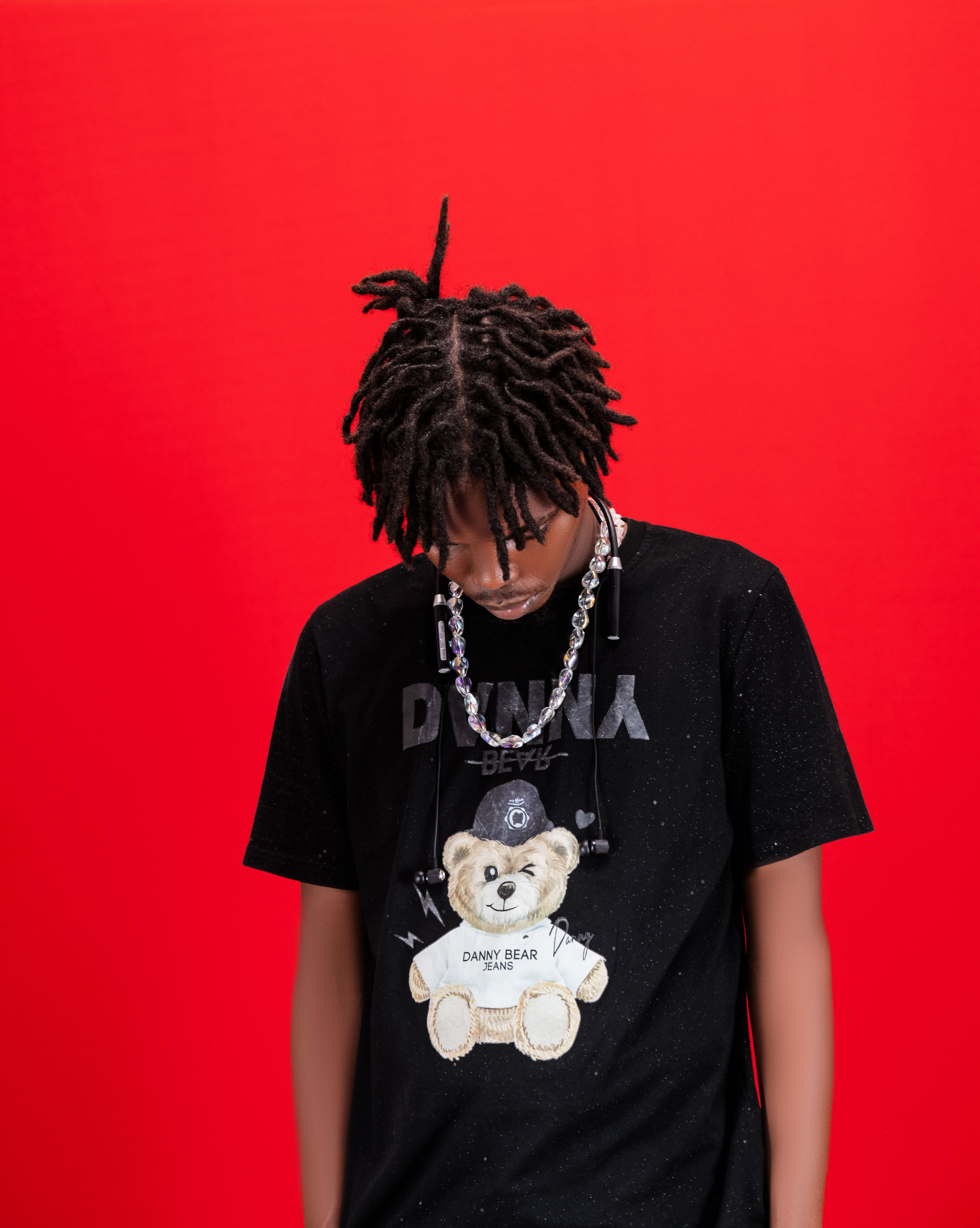 Fashionable young man wearing a black t-shirt with a teddy bear print against a vibrant red backdrop.