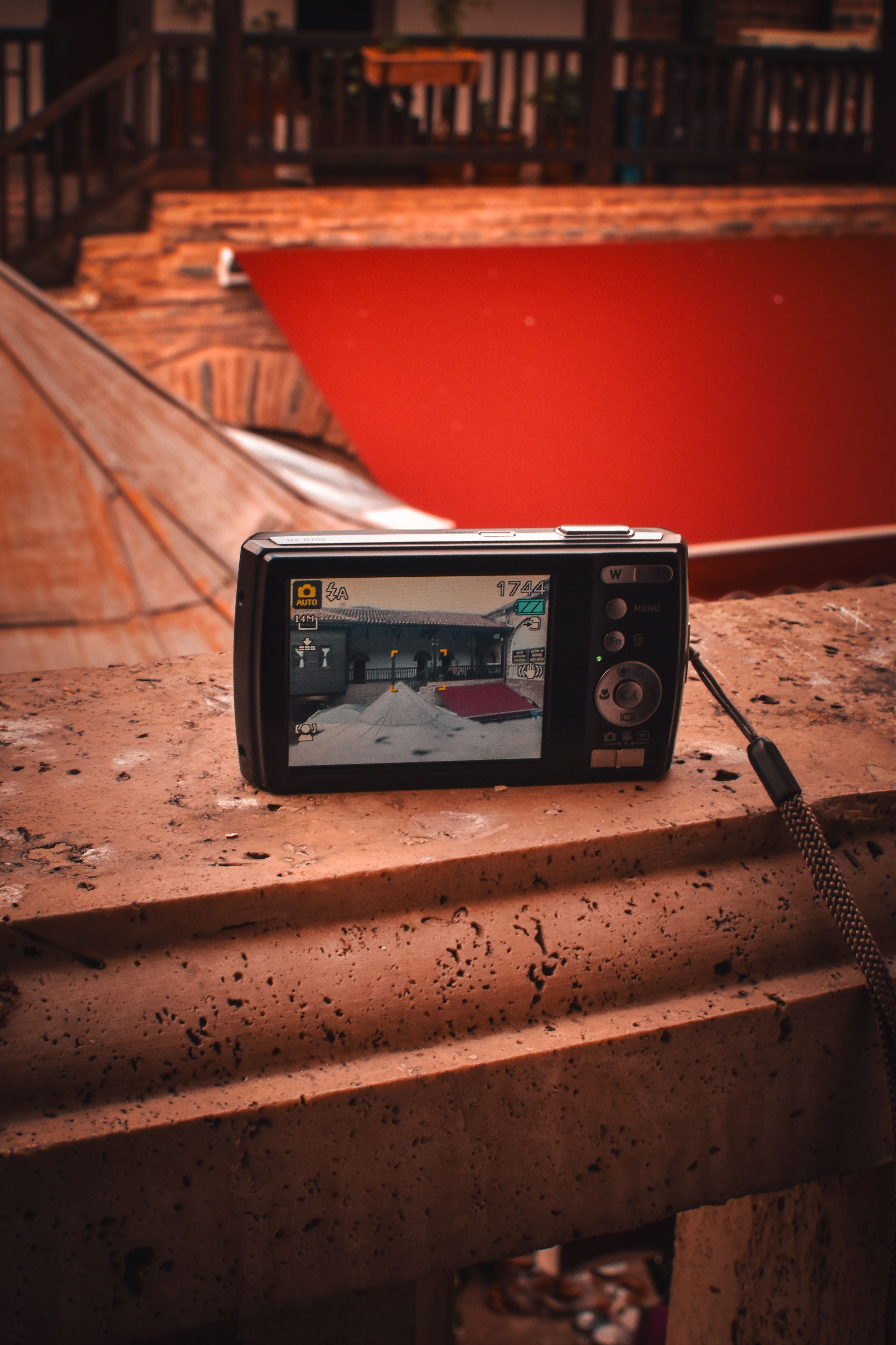 A digital camera placed on a stone railing captures the view of a rustic indoor balcony with warm tones.