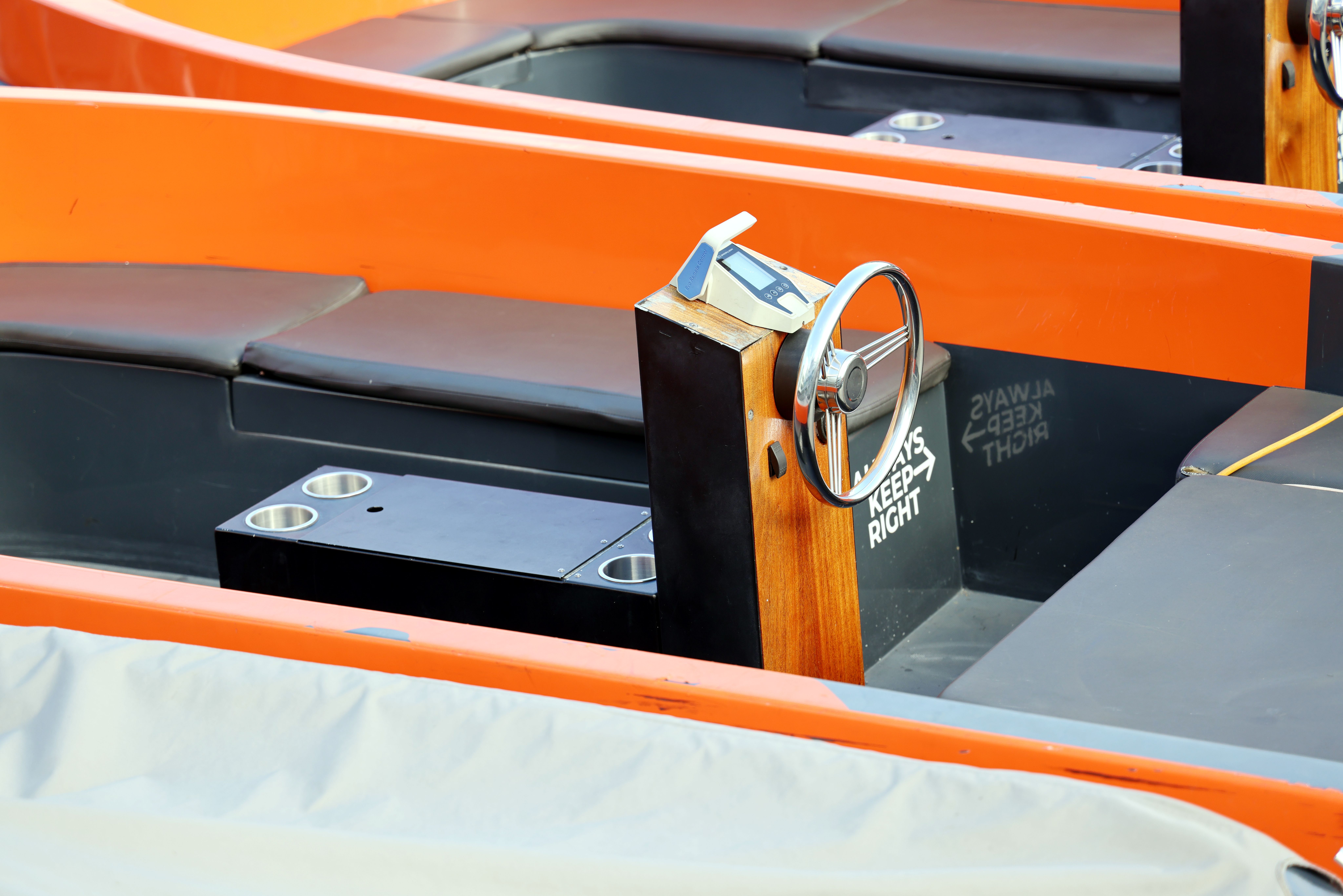 Interior of an orange boat with a wooden steering wheel and seating.