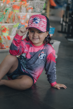 A happy child wearing a pink and gray sports outfit sitting on a floor indoors.