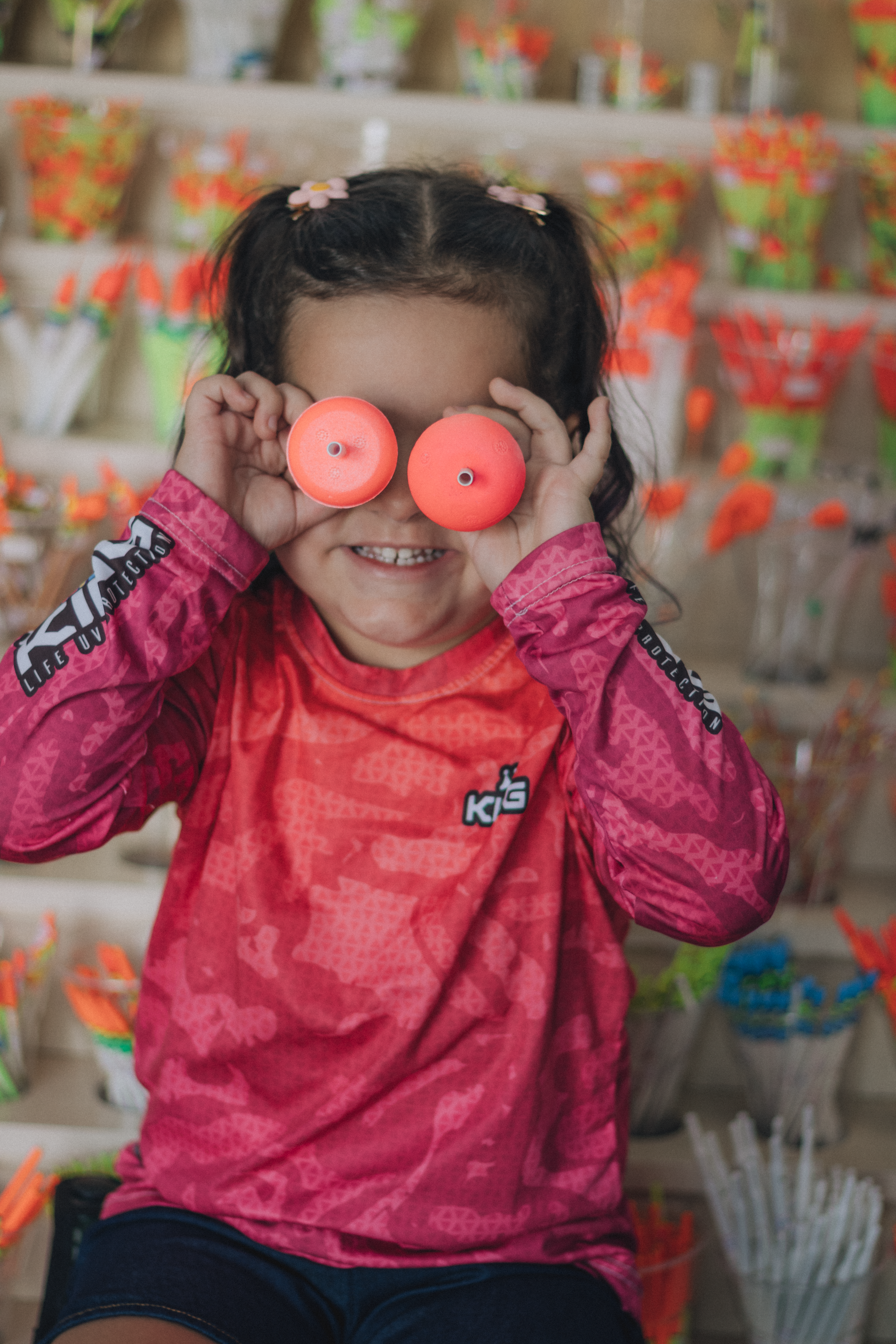 Smiling girl in pink holding colorful toy eyes. Playful and fun indoor scene.
