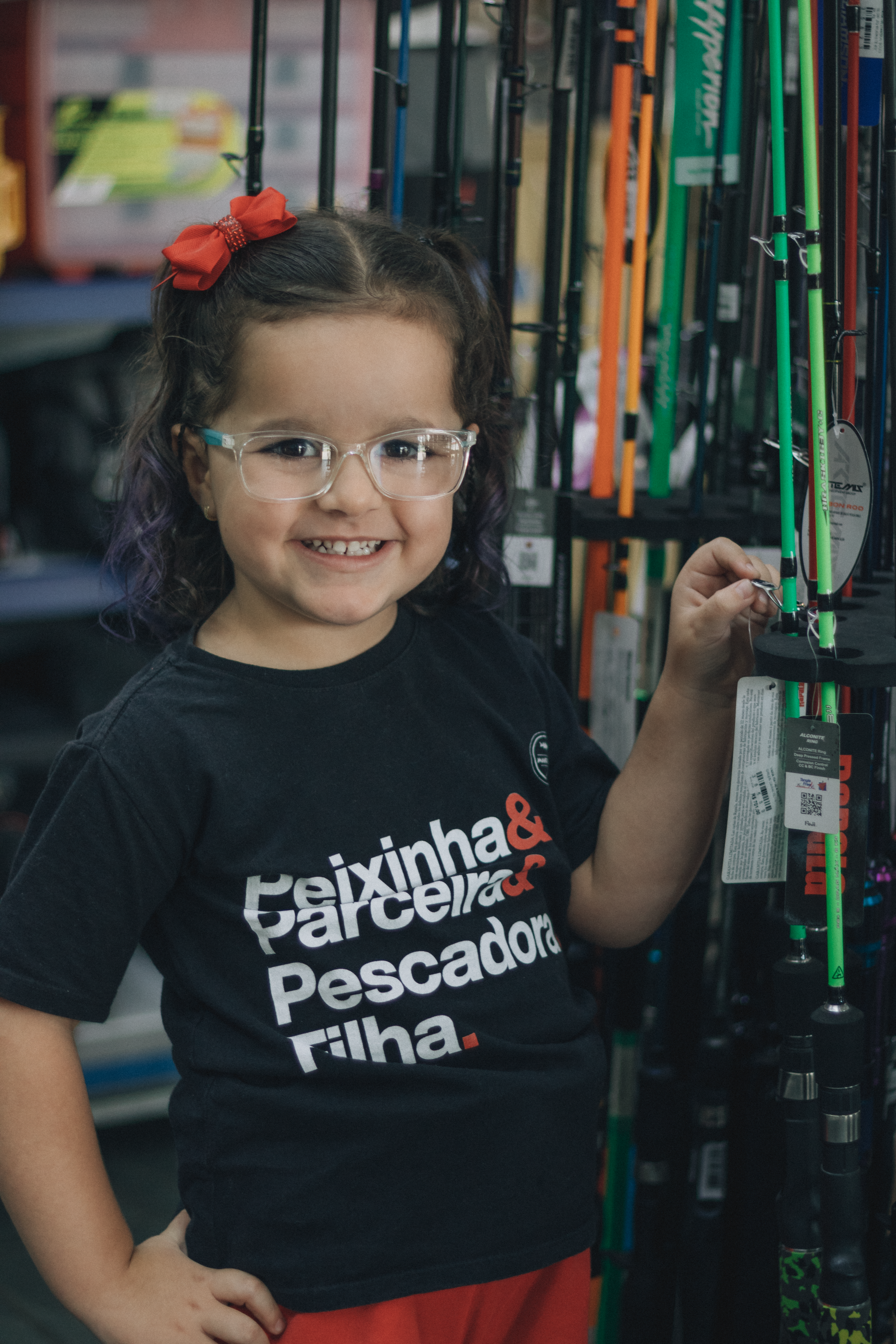 Adorable child with glasses smiling near fishing rods at a store.