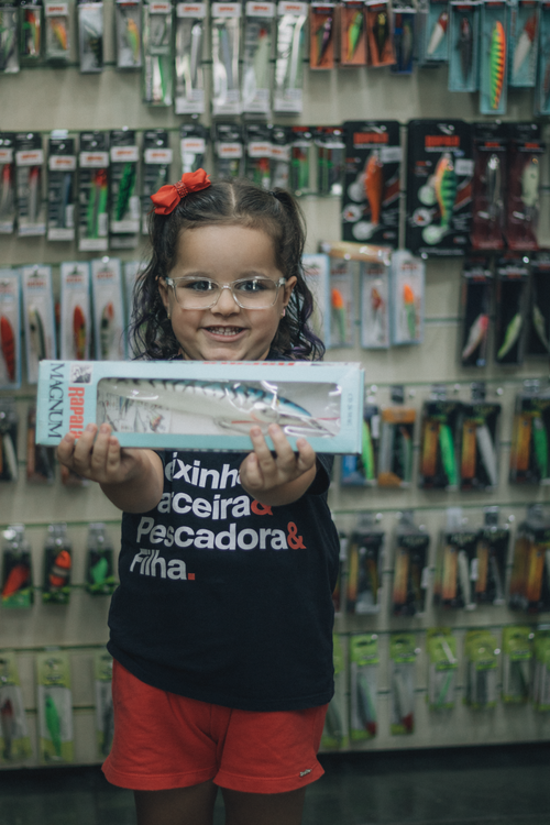 Free Young girl holding fishing lure in tackle shop with colorful packaging display. Stock Photo