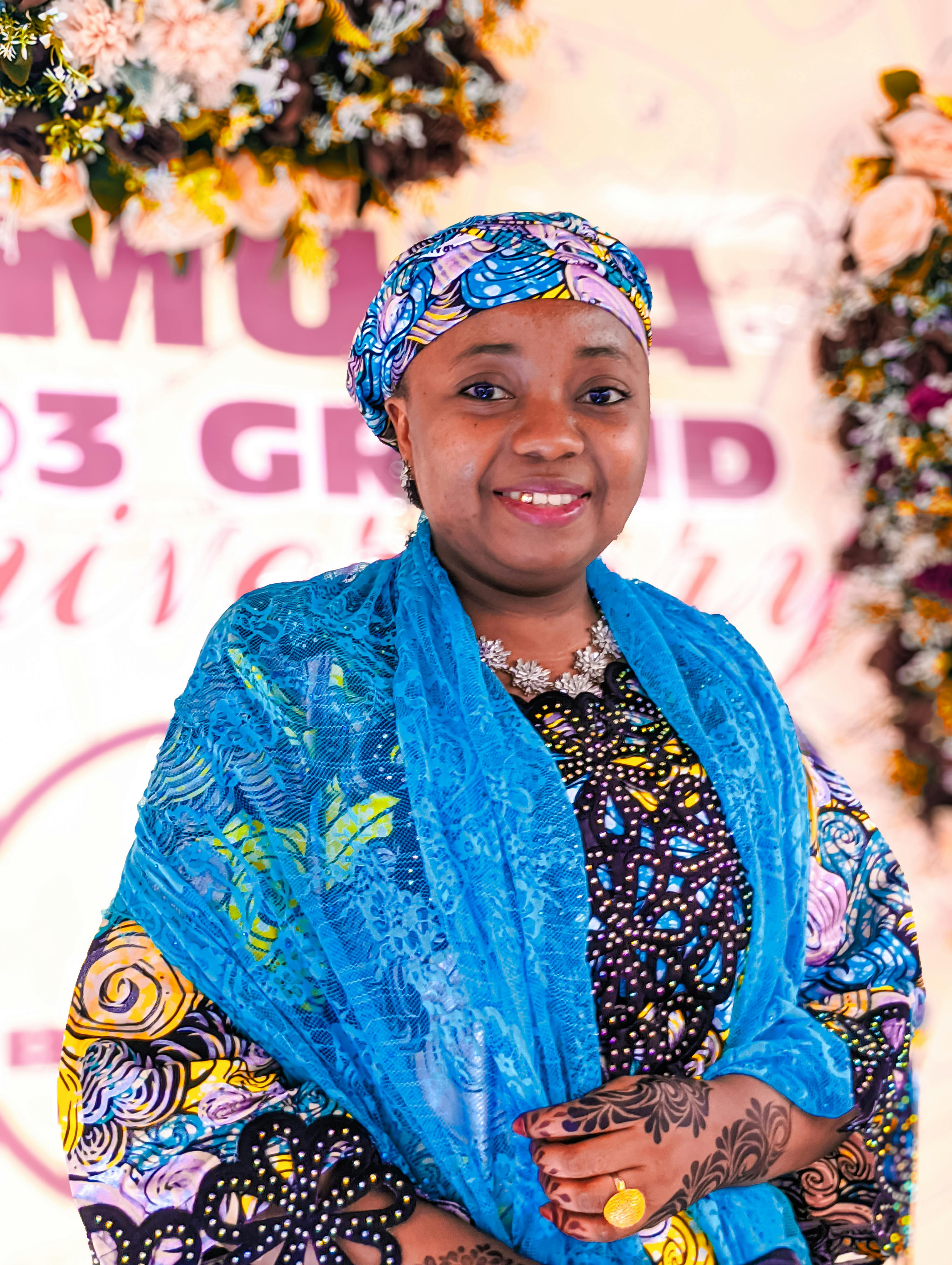 A woman smiling in vibrant traditional attire during a festive event surrounded by flowers.