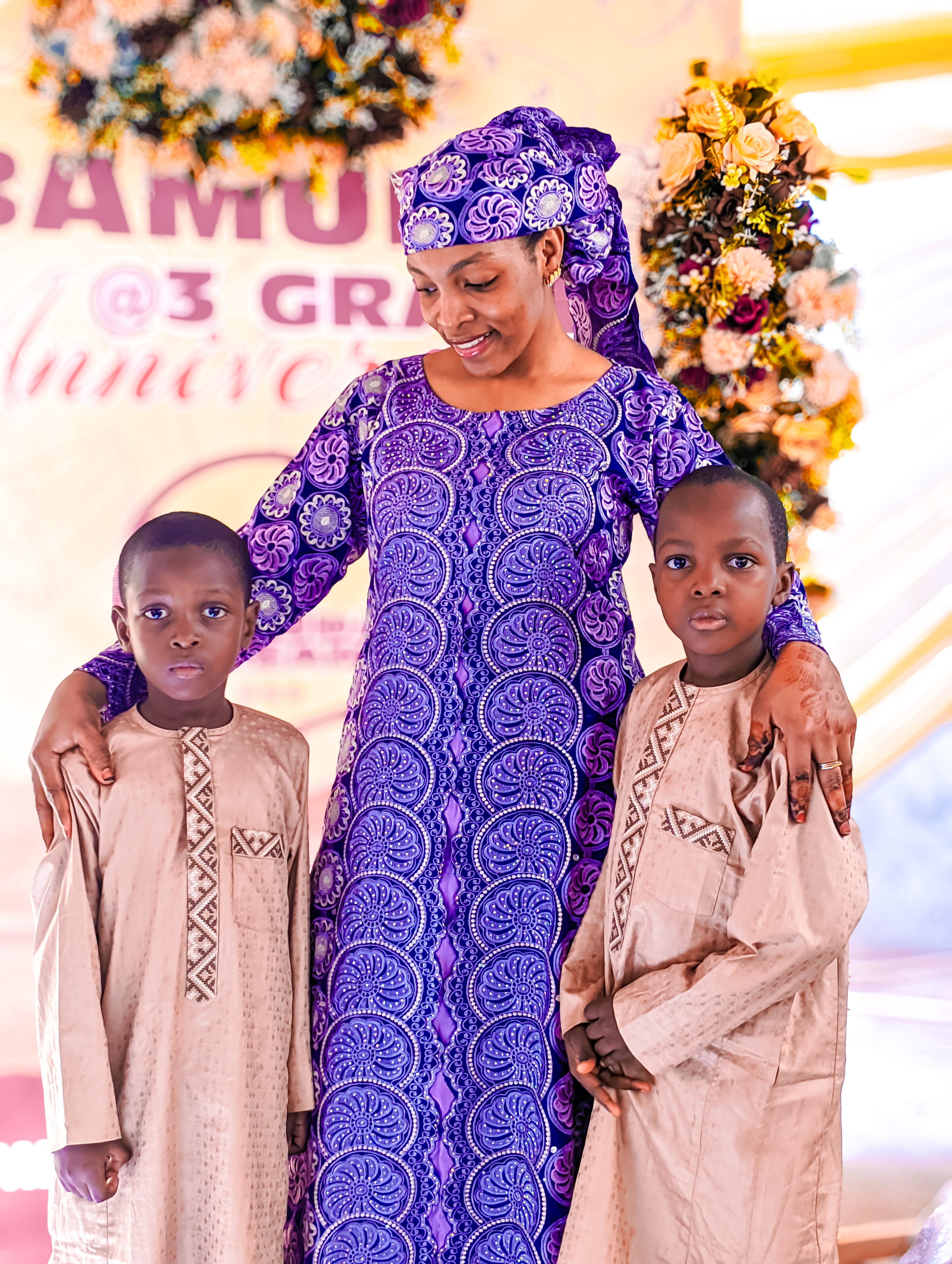 A woman and two boys in traditional attire at a celebration event.