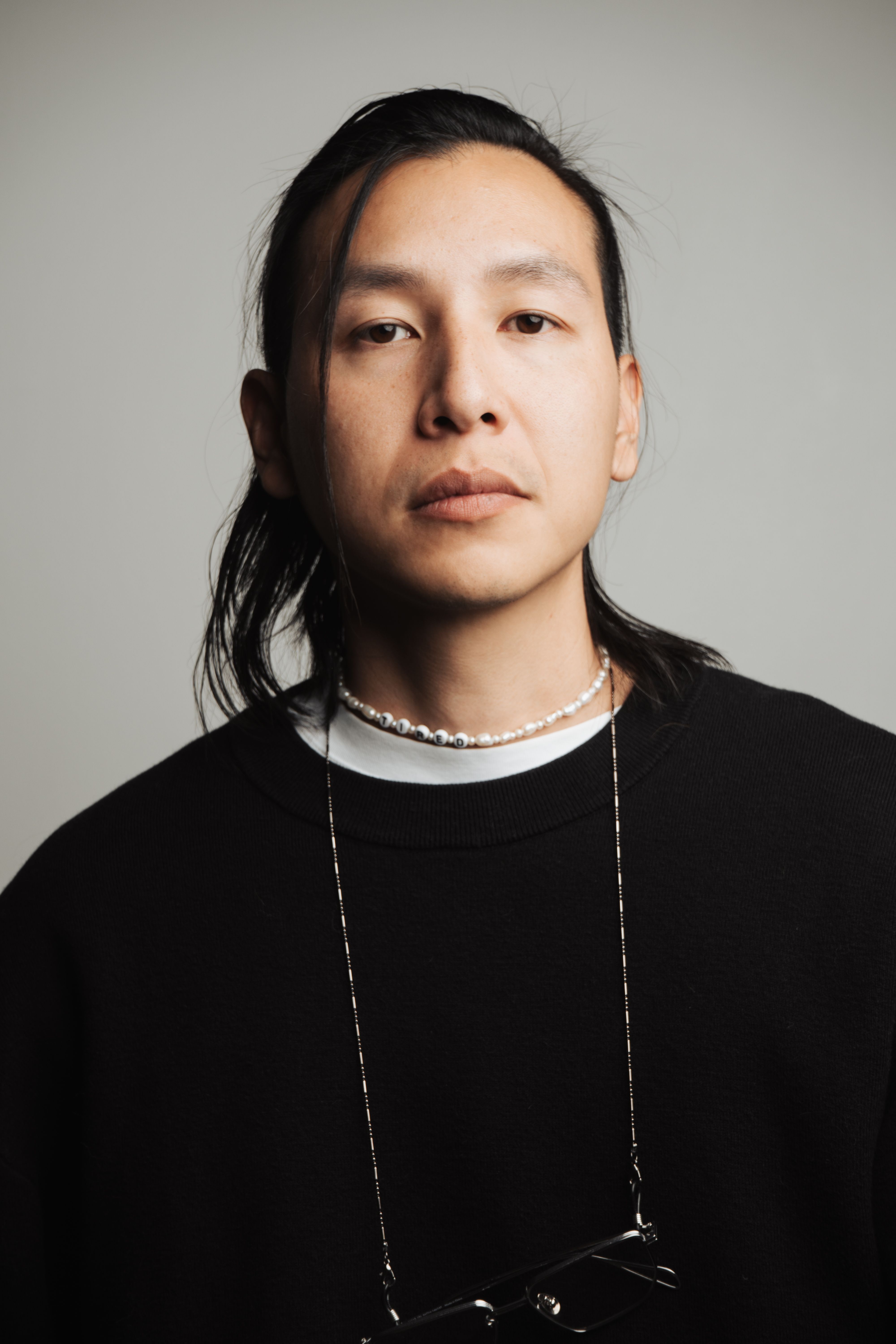 Studio portrait of an Asian adult with dark hair and minimalist fashion style.