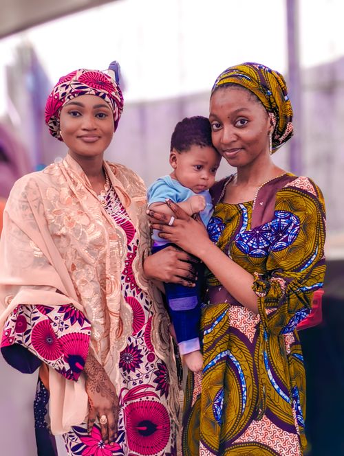 Free Two women in colorful traditional clothing holding a baby and smiling warmly. Stock Photo