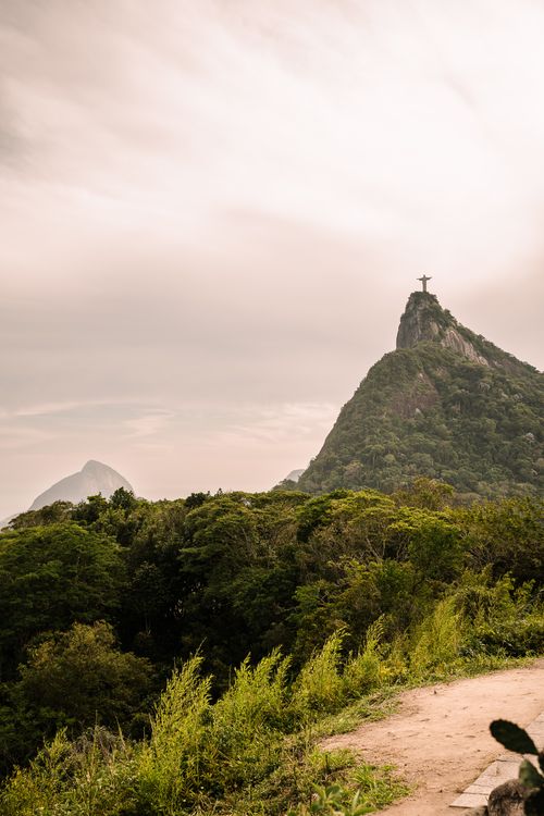 Free View of Christ the Redeemer statue on Corcovado Mountain in Rio de Janeiro with lush greenery below. Stock Photo