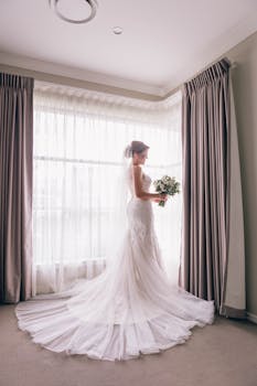 美丽的新娘穿着白色婚纱，在室内窗前摆姿势