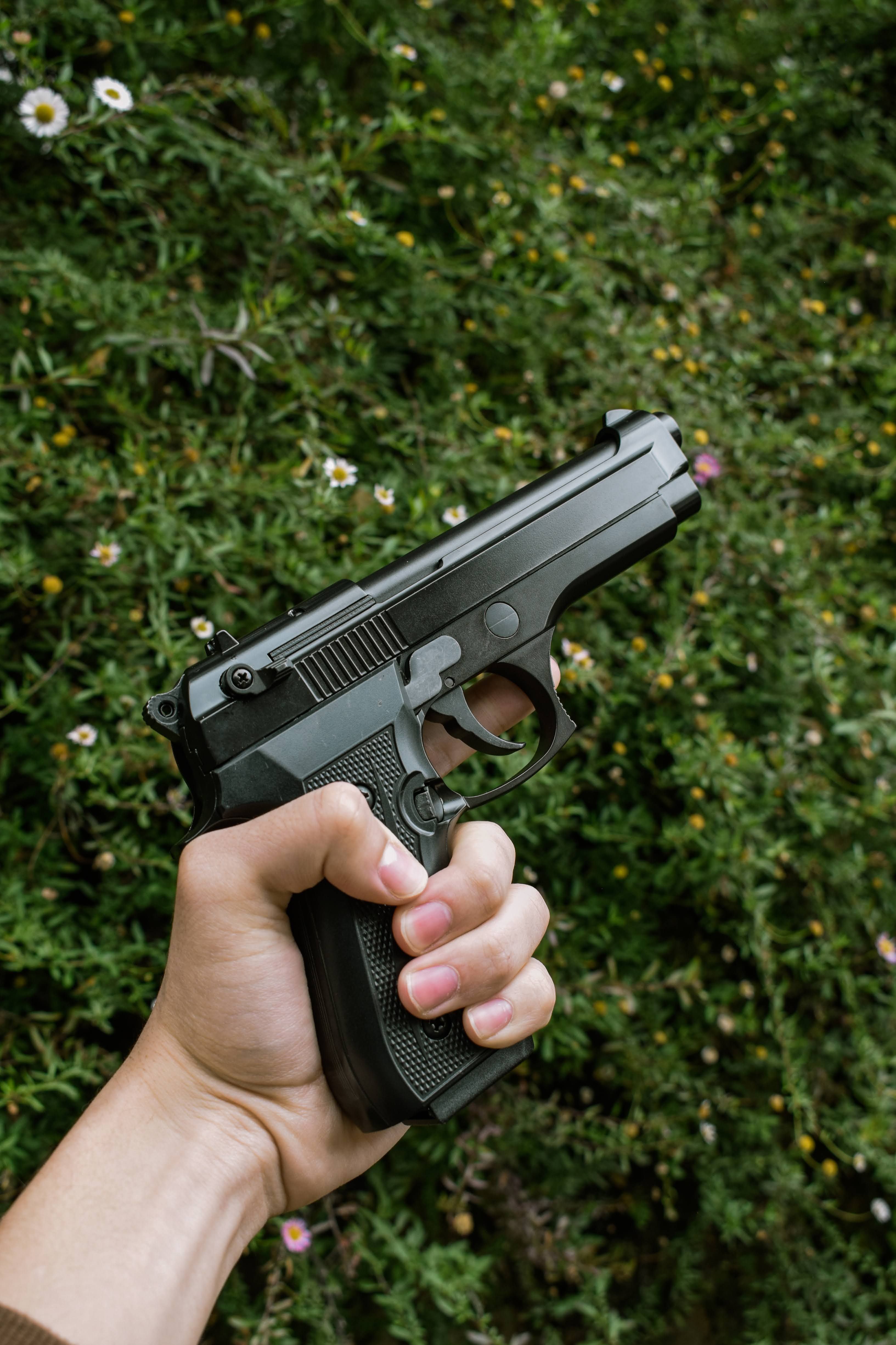 A hand firmly grips a black handgun against a lush green plant background.