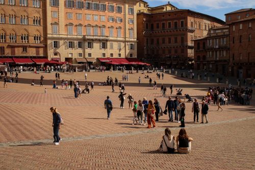 Visitantes disfrutando de un día soleado en la Piazza del Campo con forma de abanico en Siena, Italia.
