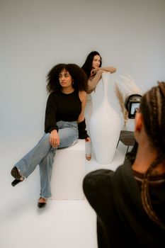 Fashionable studio portrait featuring diverse women posing stylishly with large white vase.