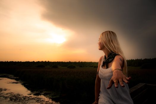 A young woman reaches out towards a serene sunset, creating a moment of connection with nature.