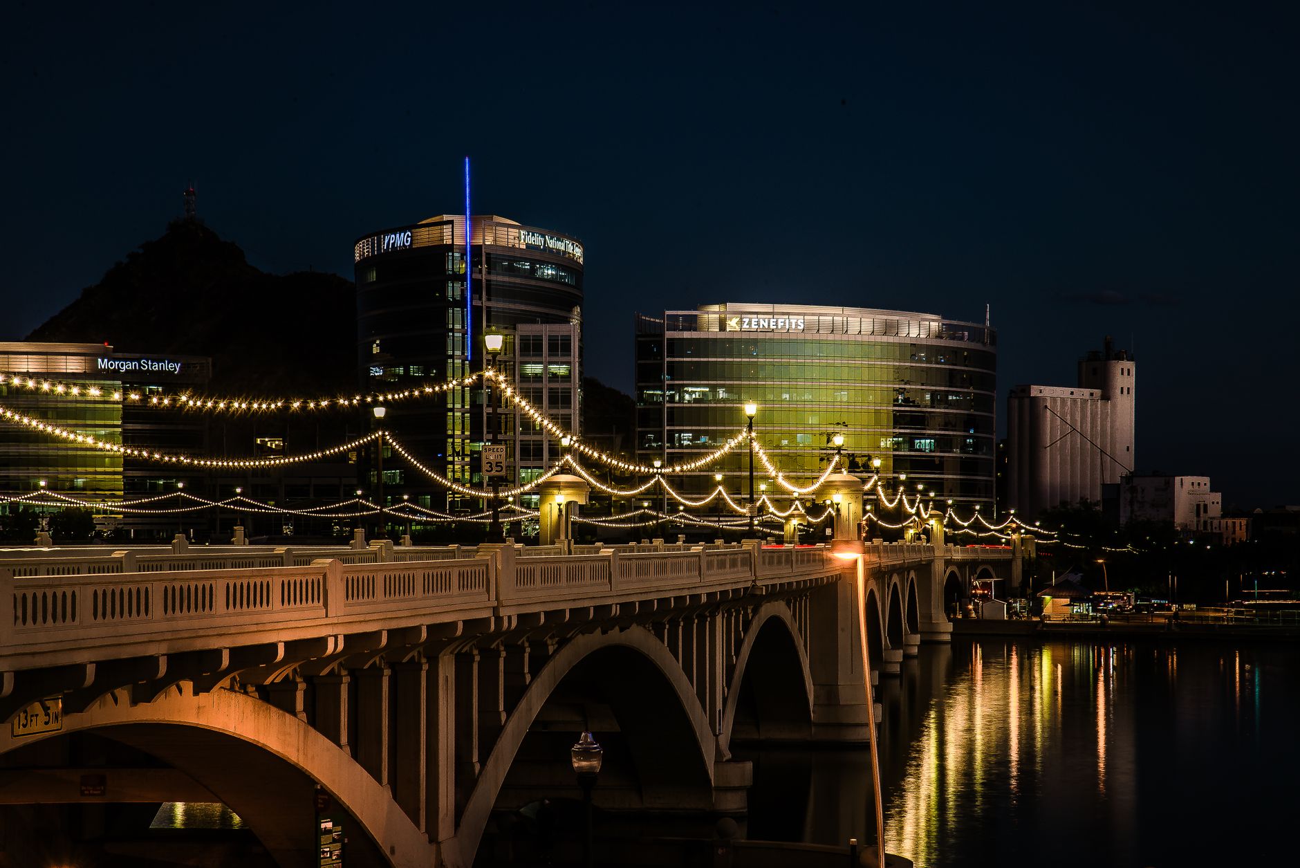 Scenic night view of illuminated bridge and cityscape in Tempe, Arizona, showcasing modern architecture and reflections.
