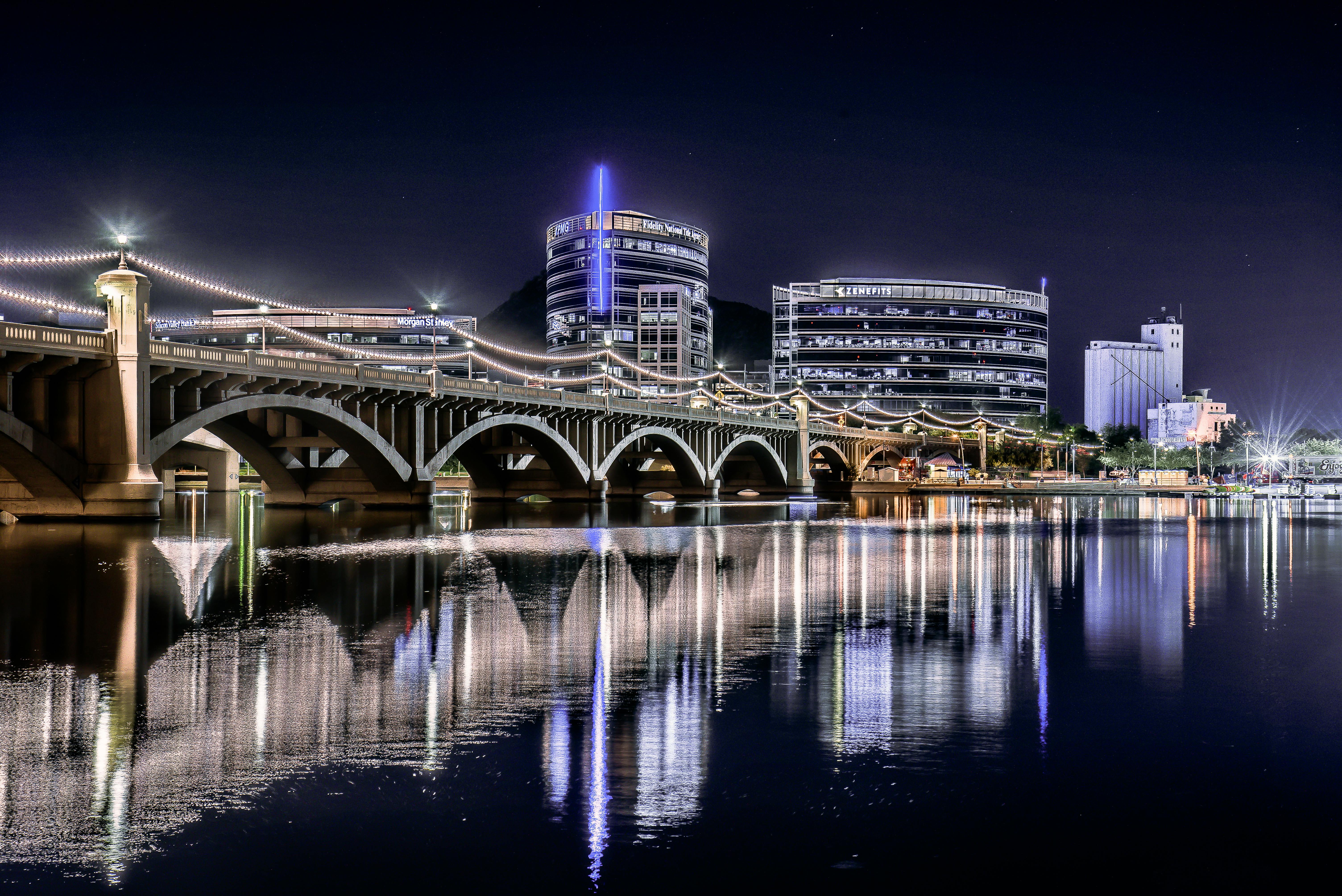 Night view of the illuminated Tempe Town Lake Bridge reflecting on the water surface.