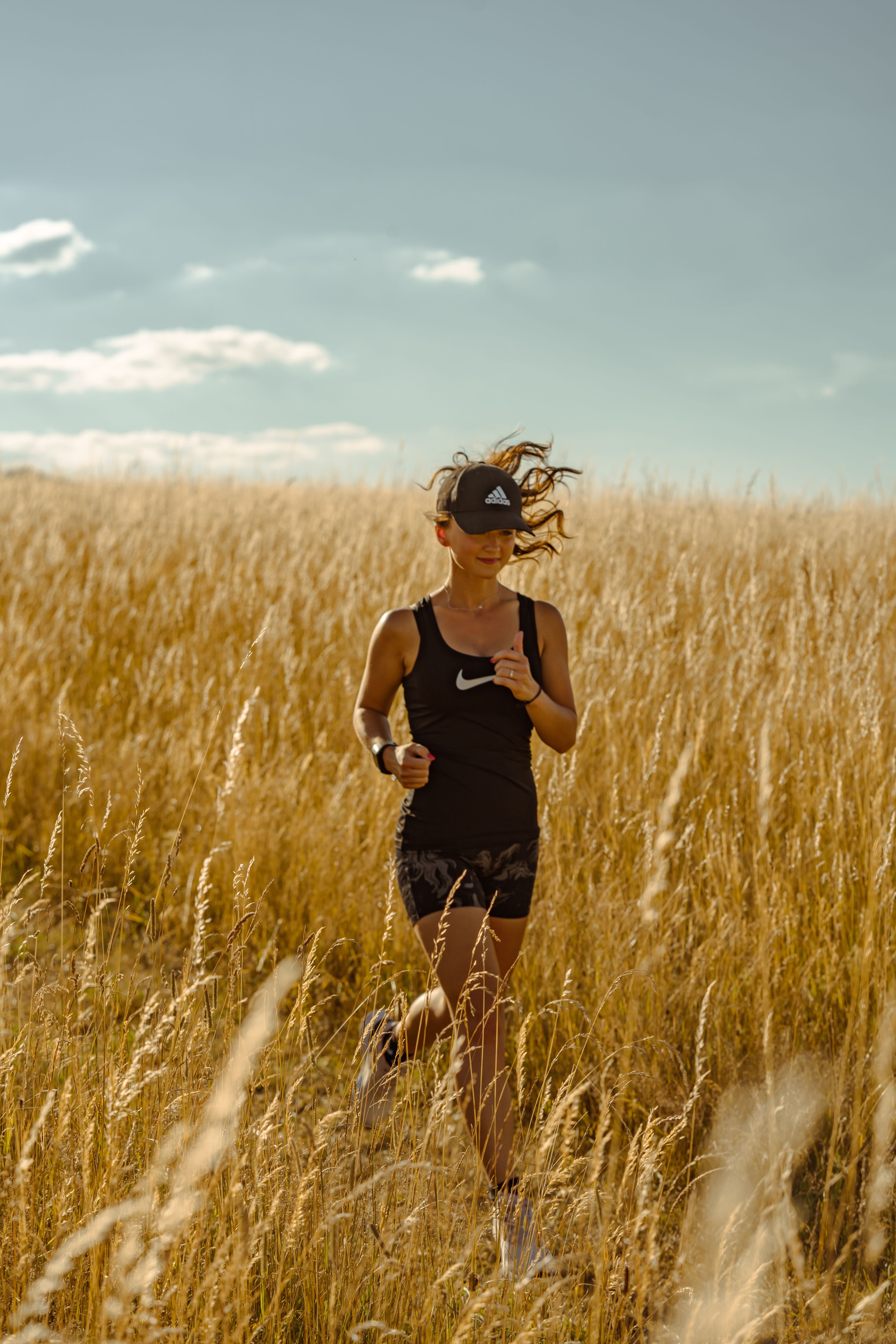 A woman in sportswear runs through a sunlit grassy field in Großschönau, Germany.