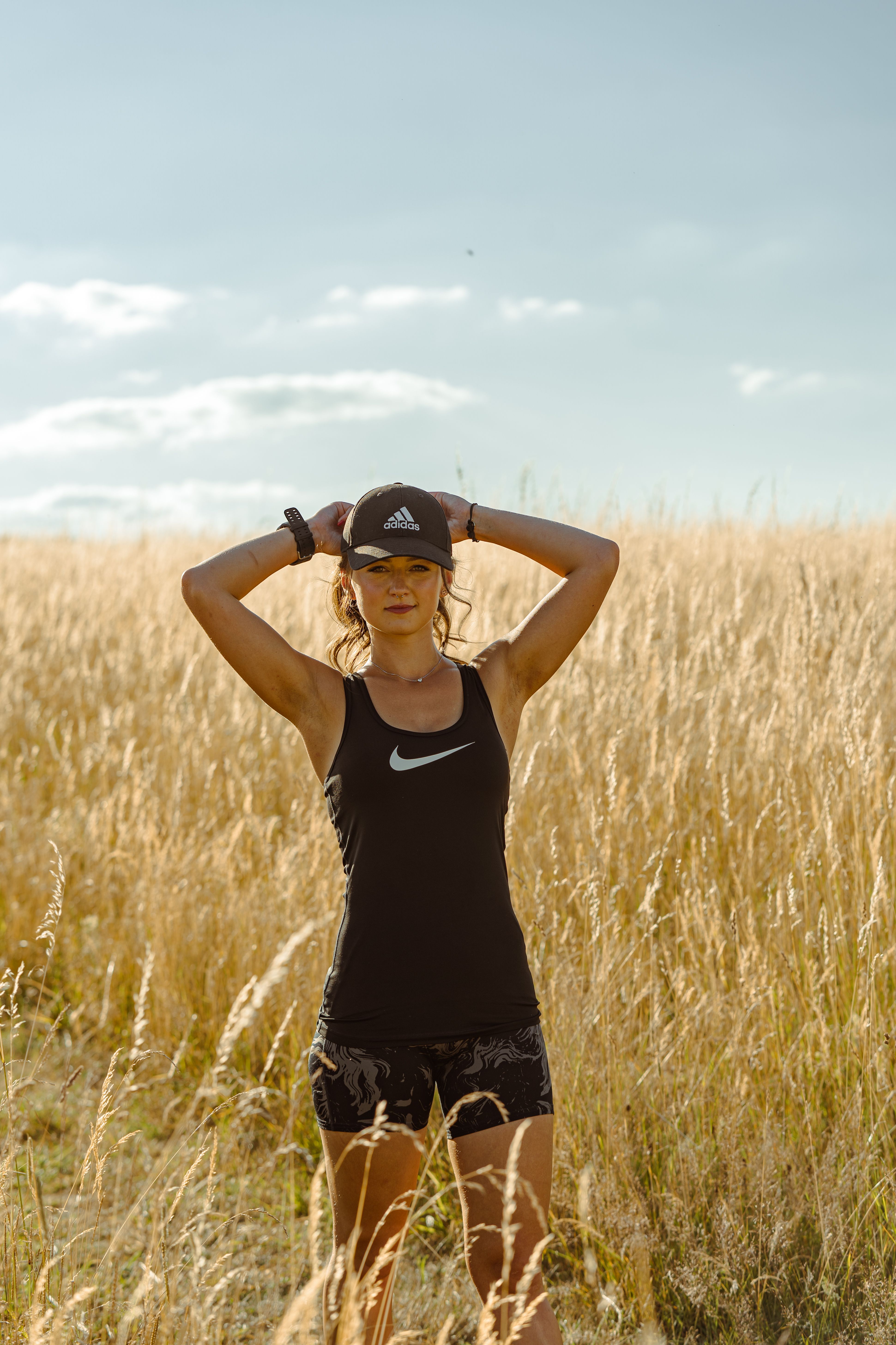 A woman stands confidently in a sunlit wheat field wearing athletic attire and cap.