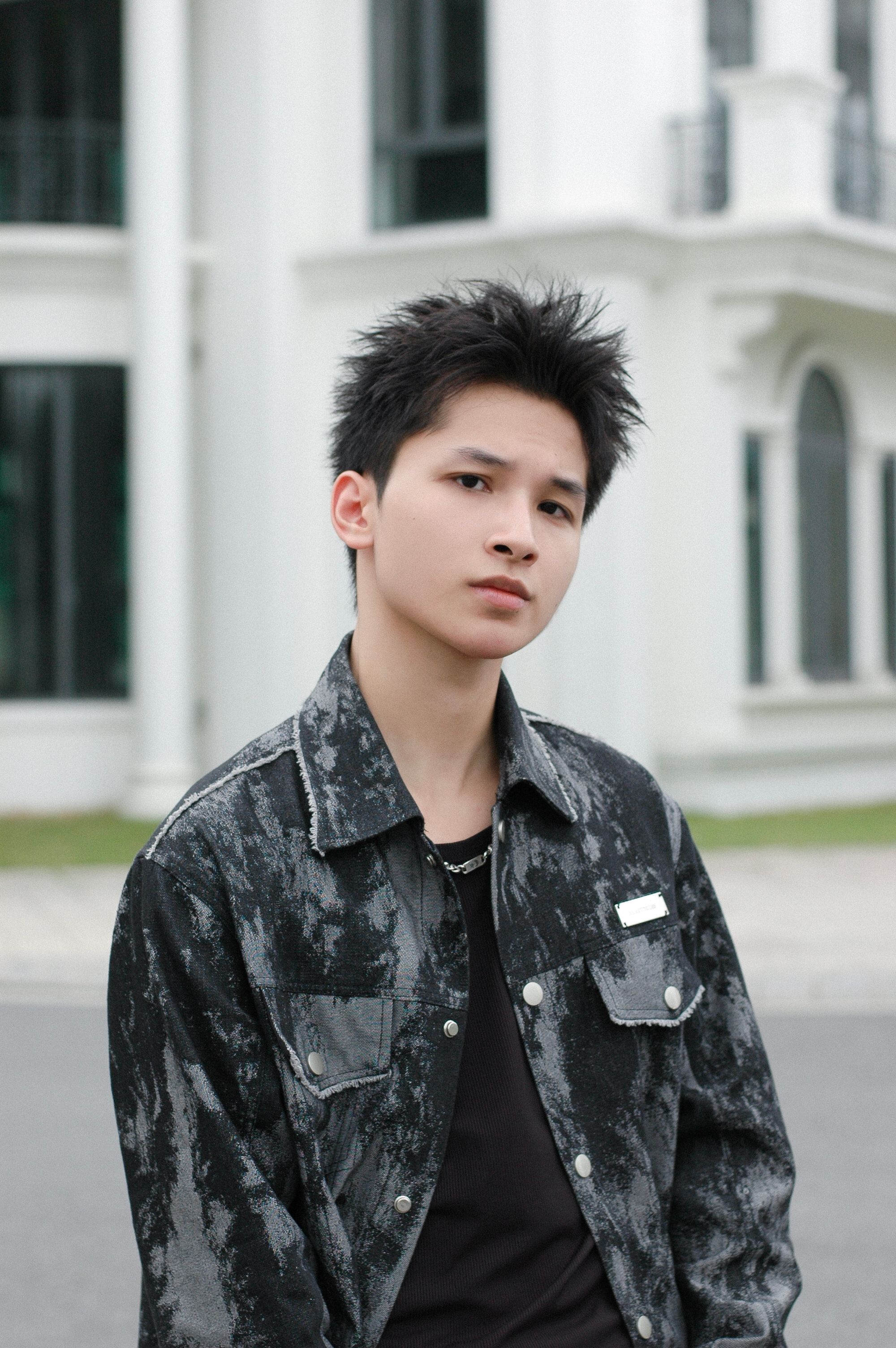 A fashionable young adult stands confidently outdoors with a modern background.