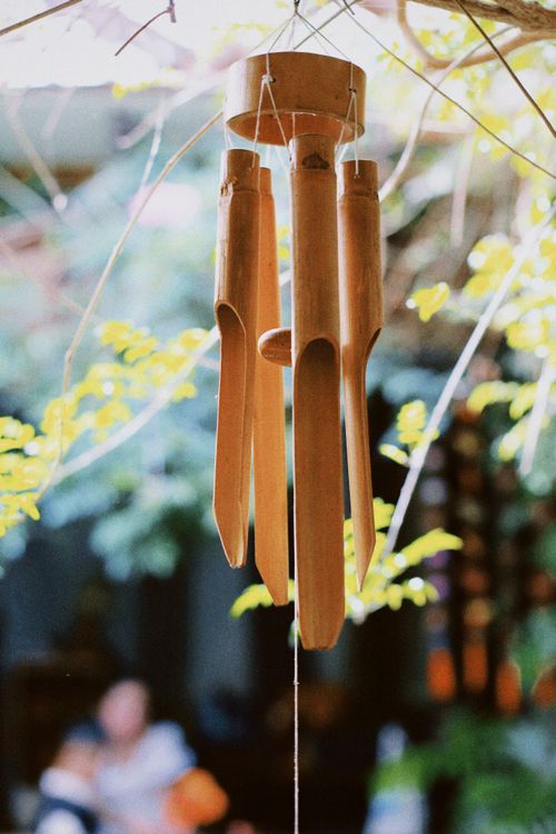 Free Bamboo wind chimes gently sway in a sunlit garden, creating a serene atmosphere. Stock Photo