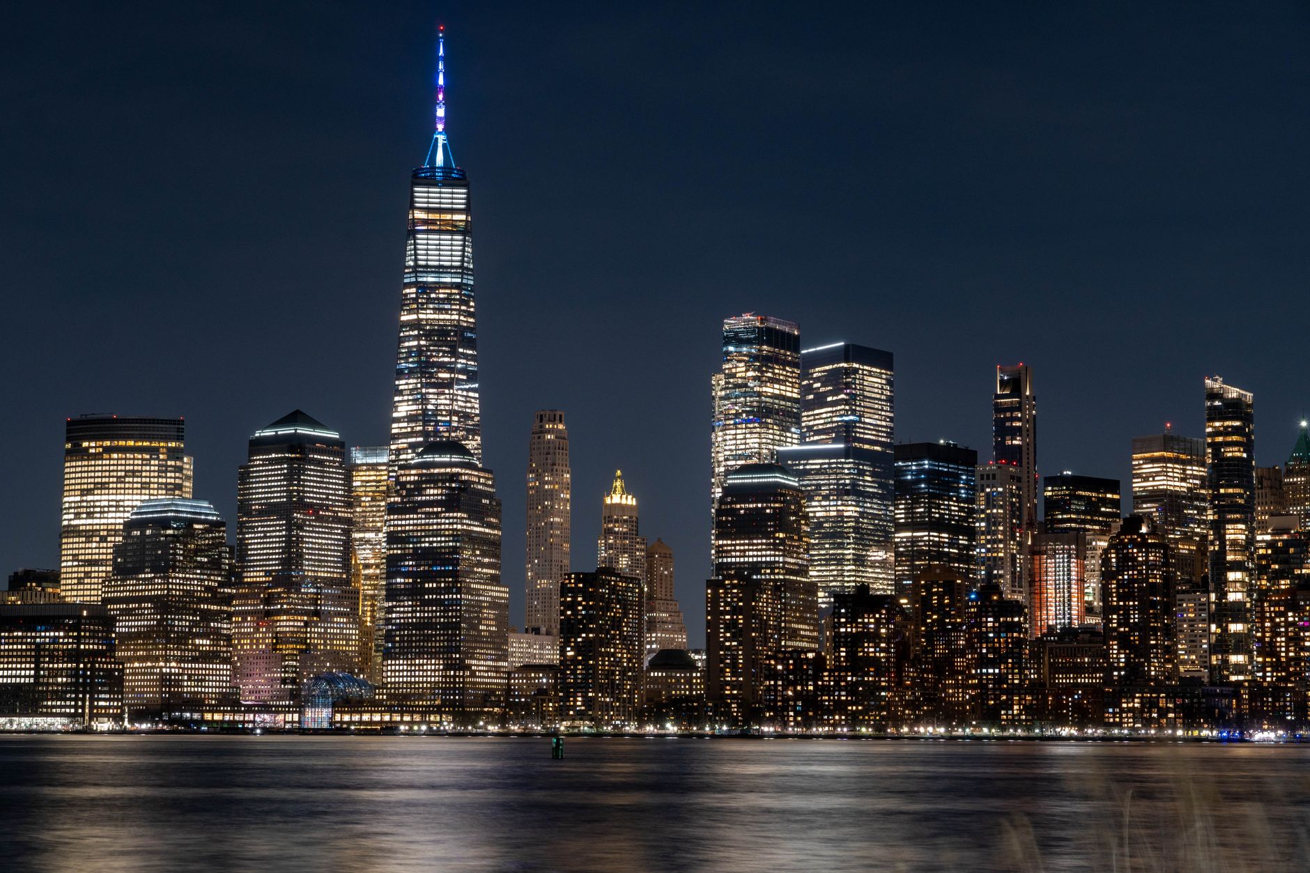 Illuminated New York City skyline featuring the iconic One World Trade Center at night.