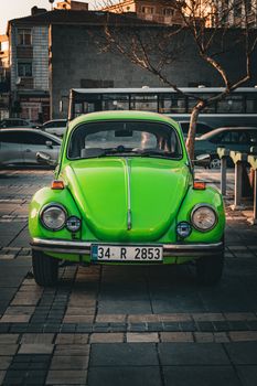 A vibrant neon green Volkswagen Beetle parked on a city street in Türkiye with shadow play at sunset.