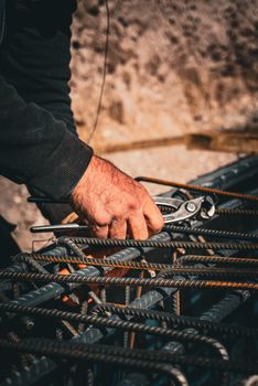 Close-up of a worker's hand using a tool to handle rebar at a construction site, showcasing rugged labor.