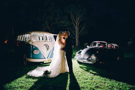 A bride and groom share a kiss beside vintage VW cars during a rustic nighttime wedding in Australia.