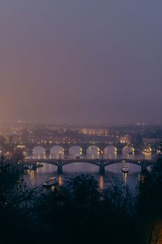 Misty twilight scene of the Charles Bridge in Prague, illuminated over the Vltava River.