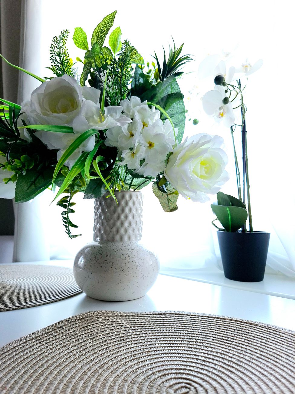 White and green floral arrangement in a ceramic vase catching natural window light