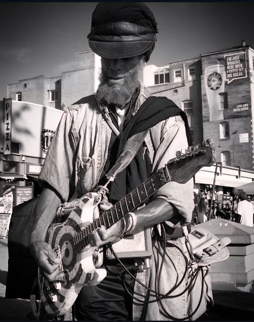 Free Black and white photo of a street musician playing guitar outdoors in an urban area. Stock Photo