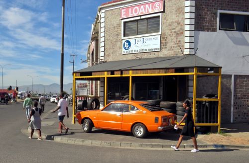 Free A vintage orange car parked outside a brick building with a tire shop, capturing urban street life. Stock Photo