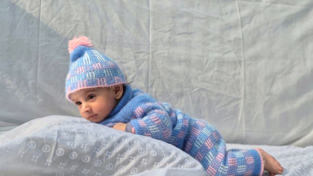 Cute baby wearing a cozy knitted outfit with pastel colors, lying indoors on a soft surface.