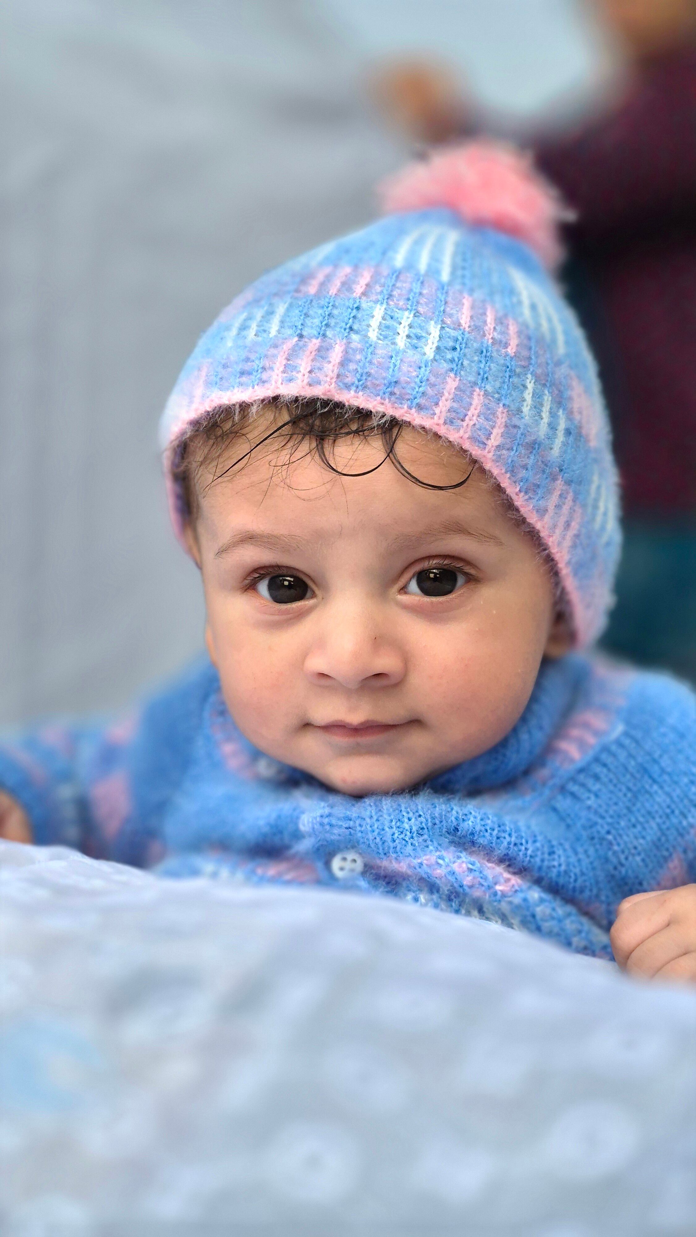 Cute baby wearing blue knit hat and sweater, looking at camera.