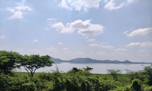 Peaceful lake view with lush greenery and mountains under a blue sky.