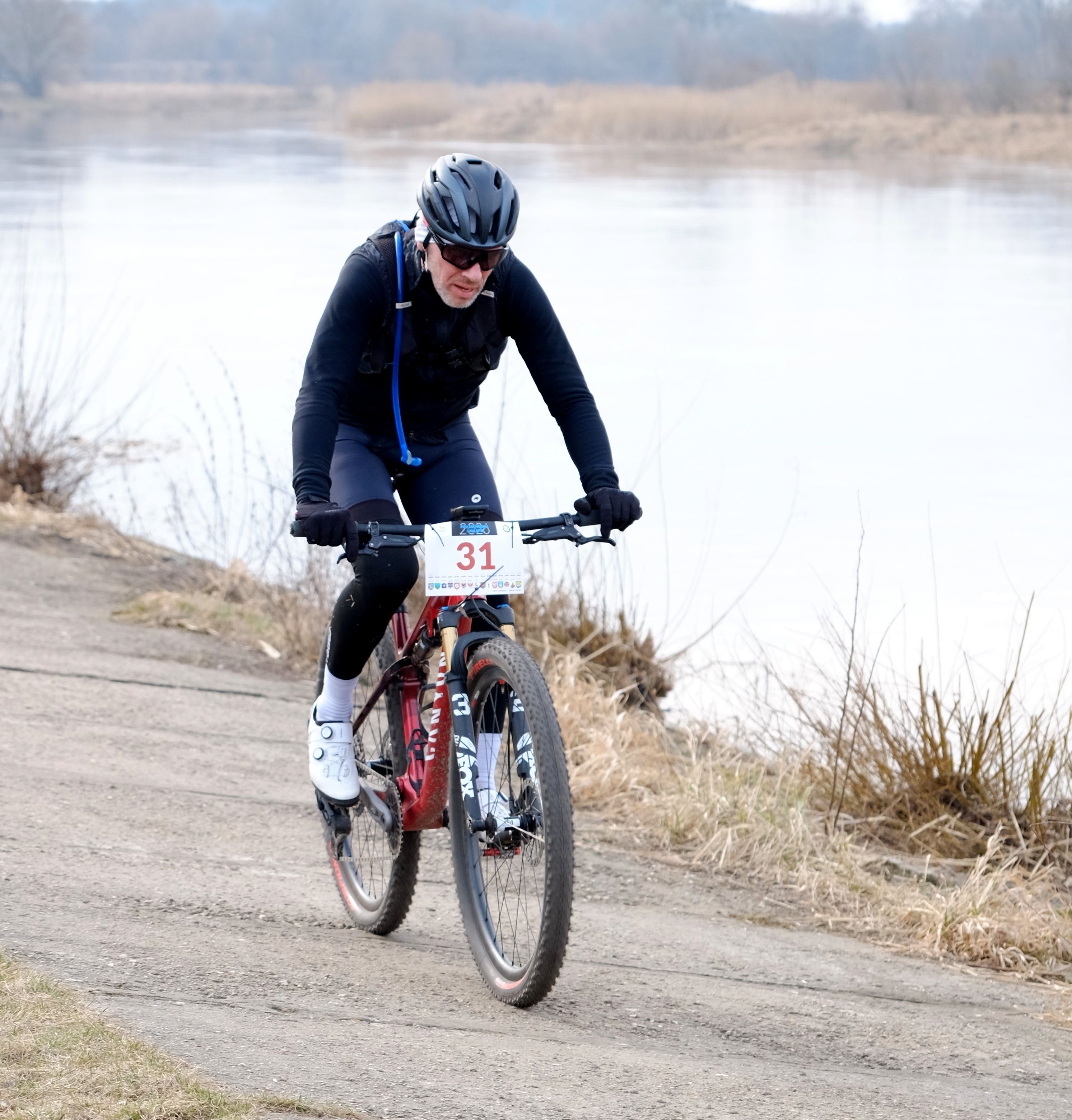 Professional cyclist riding along a riverside path in a competitive race, showcasing endurance and determination.