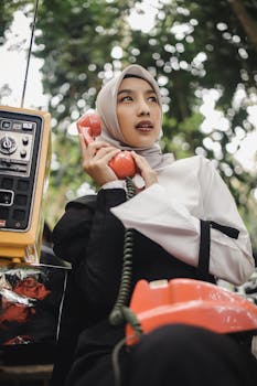 Young woman in a hijab talking on a vintage phone outside in Bandung, Indonesia.