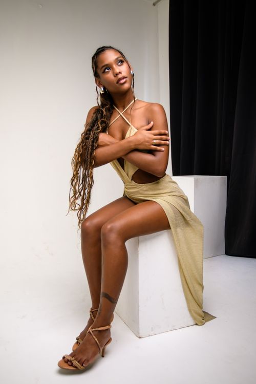 Free An elegant woman in a gold dress poses thoughtfully in a modern studio setting. Stock Photo