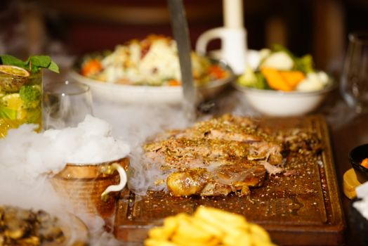 Delicious roasted meat on a wooden board served with vegetables and fries in a warm setting.