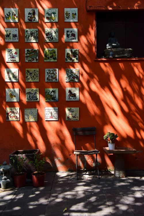 Free Sunlit orange wall with artwork tiles, shadows, chair, and decor creating an artistic outdoor scene. Stock Photo