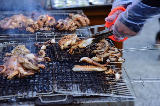 Vibrant outdoor scene of grilled octopus being prepared with tongs. Perfect for culinary themes.