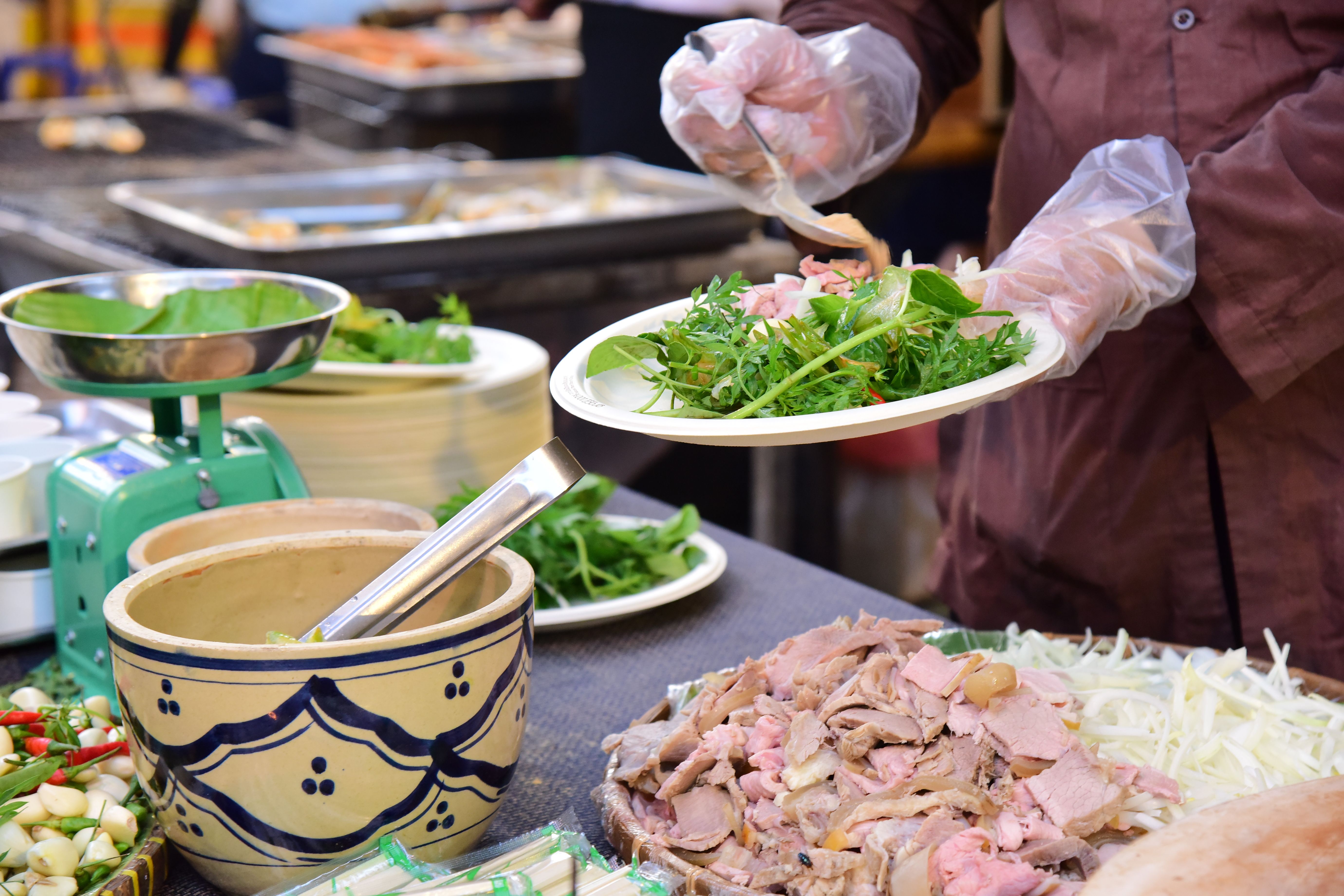 colorful street food market with students eating at a plastic table, vibrant dishes in the foreground